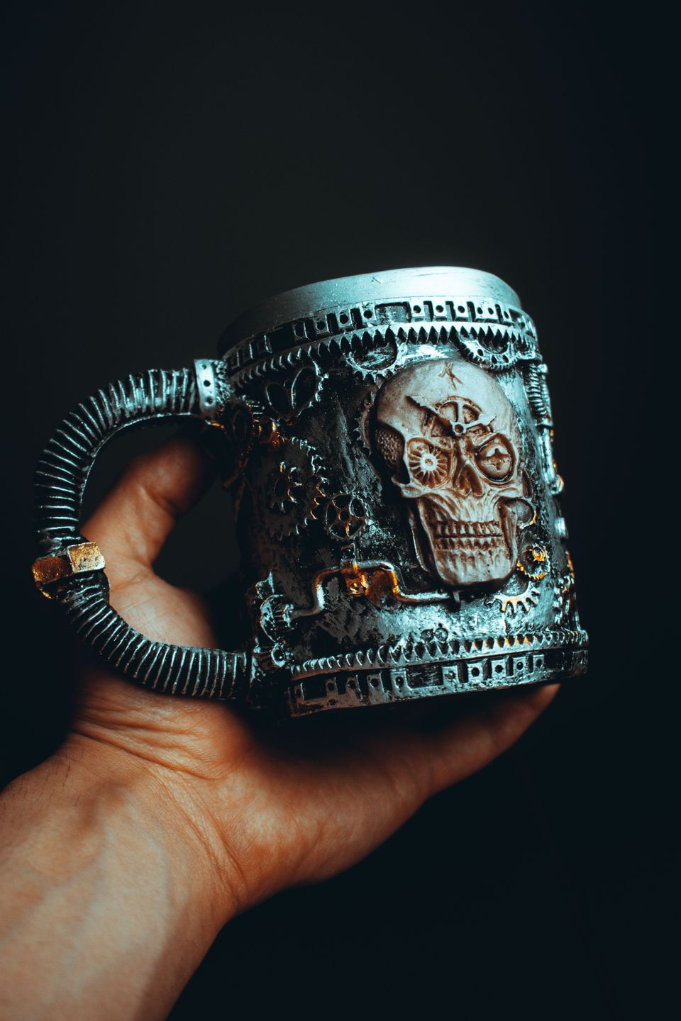 Hand holding a silver sculpted tankard decorated with gears, pipes and a clockwork skull relief