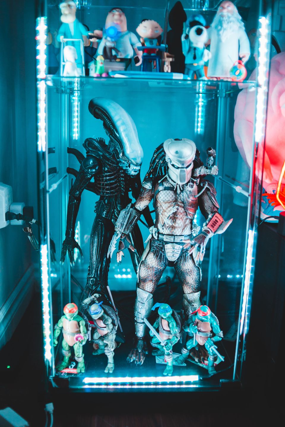 Glass display cabinet lit with cool LED strips holding large creature figures and smaller action figures