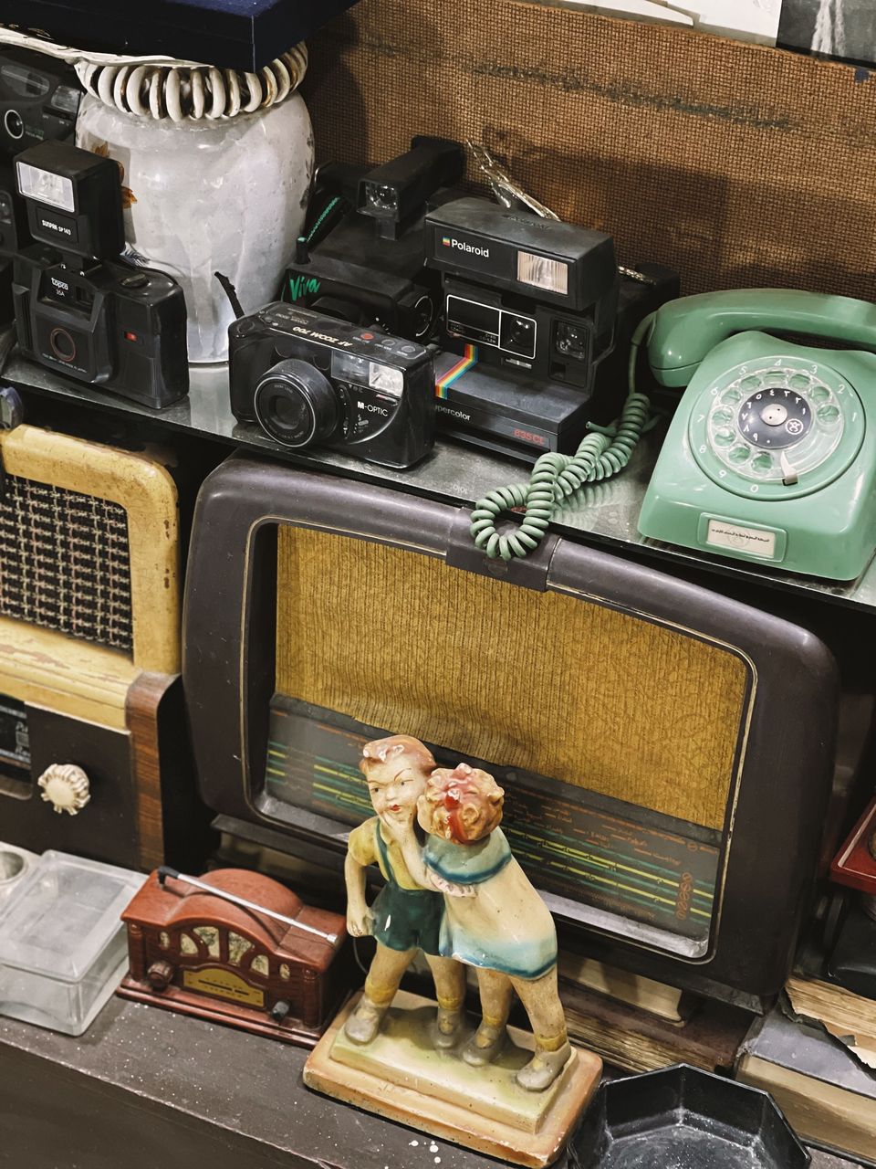 Shelf of vintage tabletop radios, compact film cameras and a green rotary telephone
