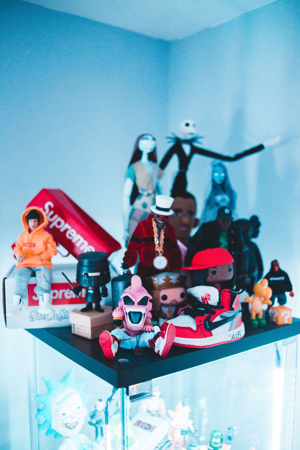 Corner shelf with streetwear-styled figures, a miniature red sneaker and vinyl figures, with tall stylized figures behind