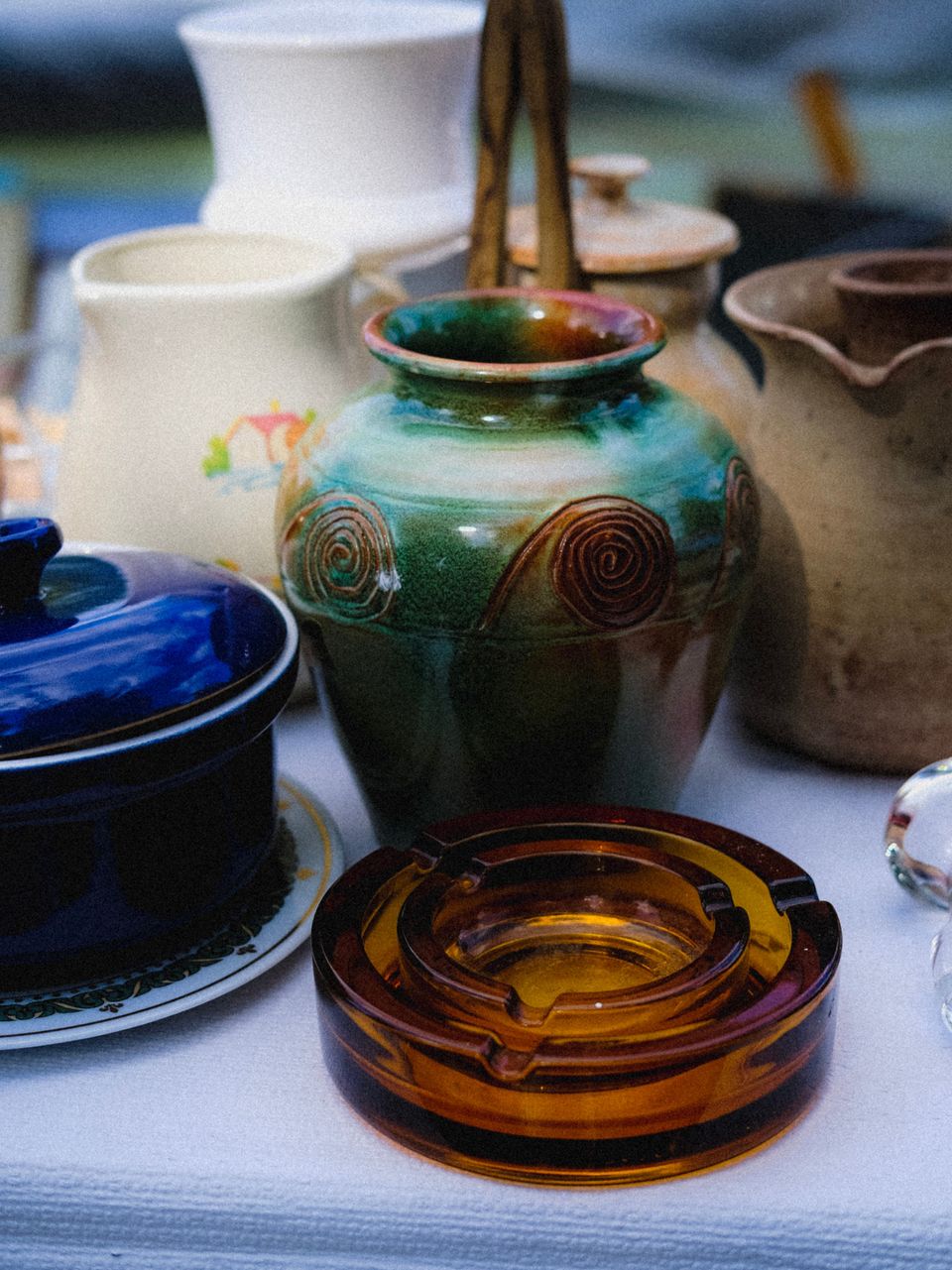 Green and amber glazed pottery vase with raised spirals, an amber glass dish and a blue lidded dish in front