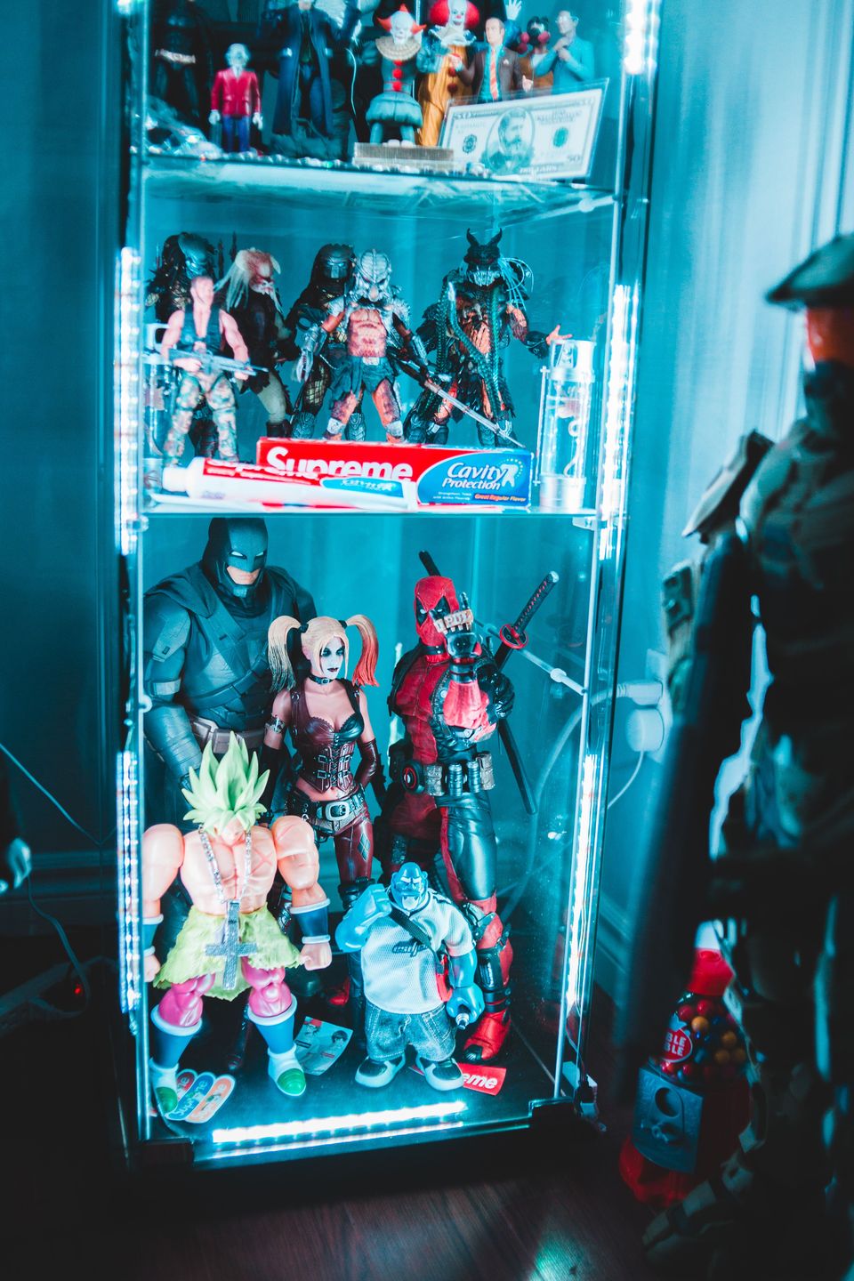 Three-shelf glass cabinet of posed action figures lit by blue-white LED strips