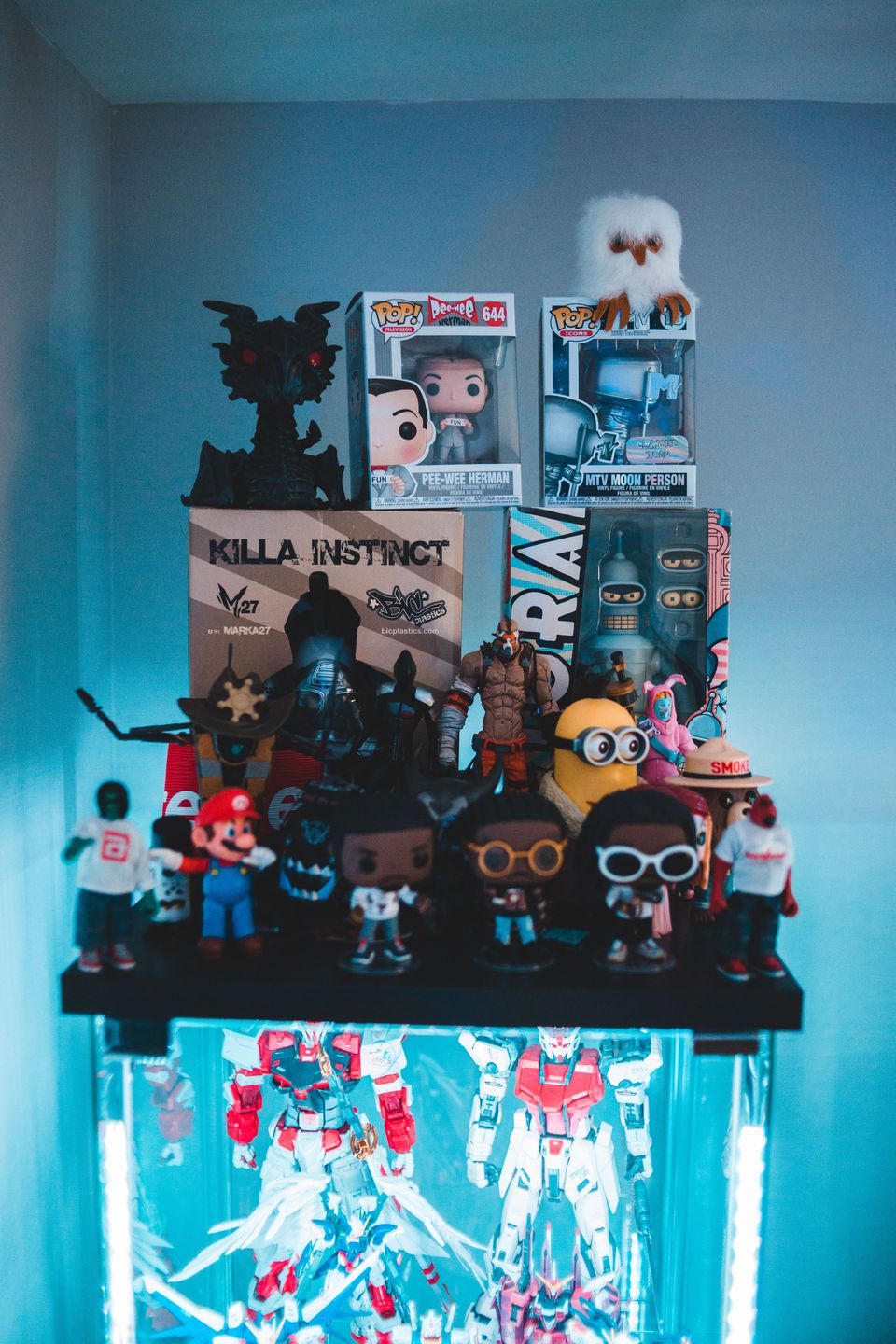 Shelf-top arrangement of boxed and loose vinyl figures above an illuminated cabinet of white and red model kits